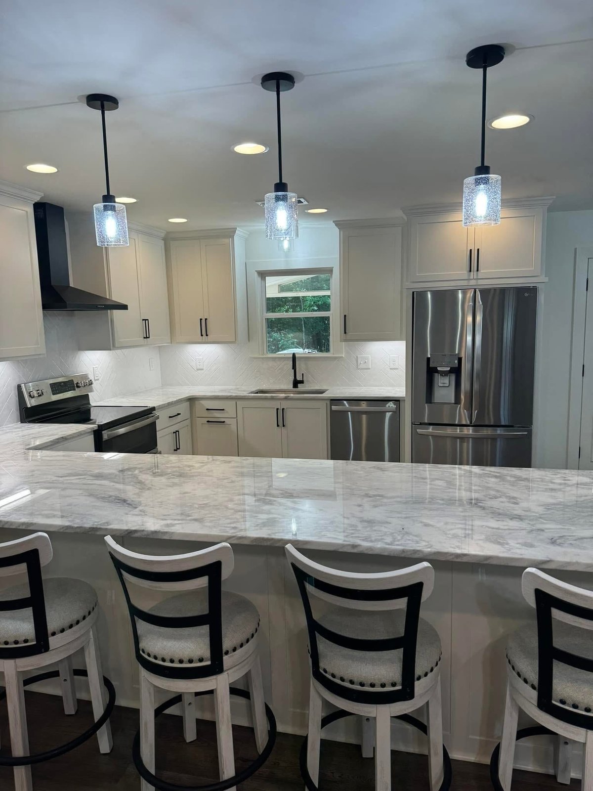 Modern kitchen with white cabinetry, marble countertop island, stainless steel appliances, and pendant lighting